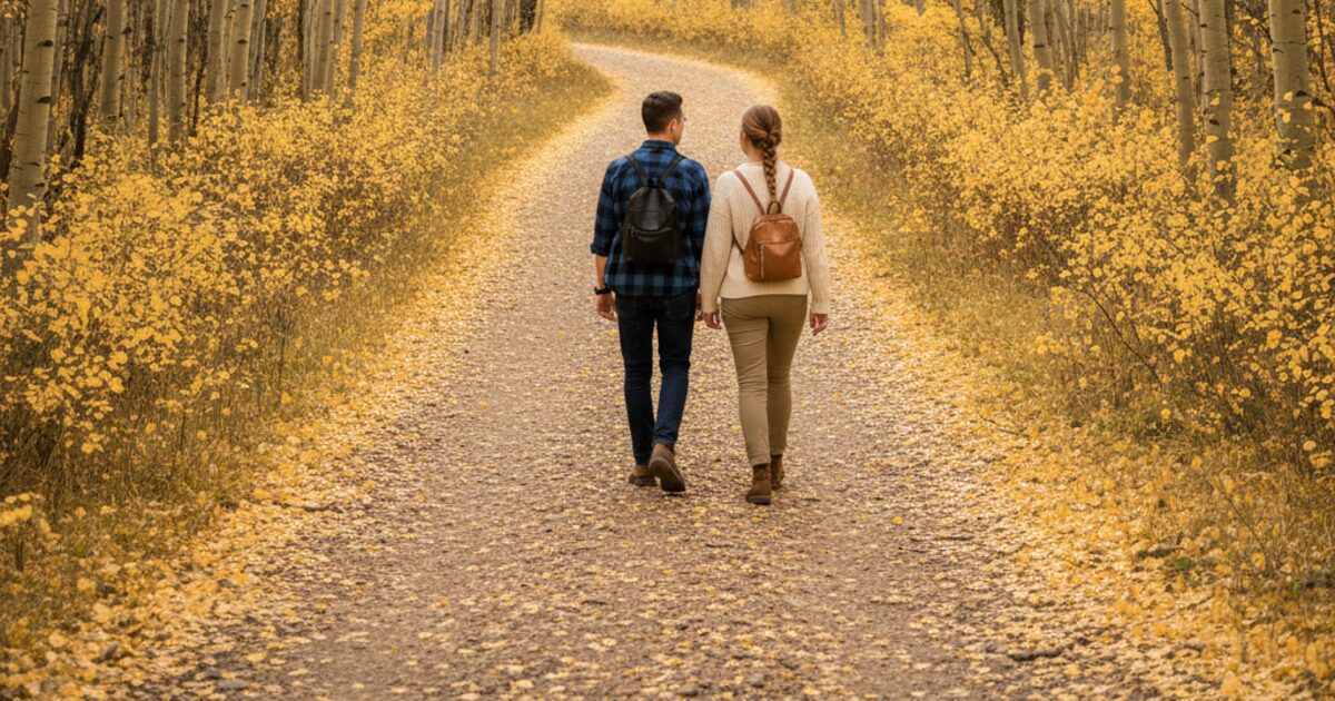 Two people seen from behind walking on a gravel trail through golden aspen trees in autumn